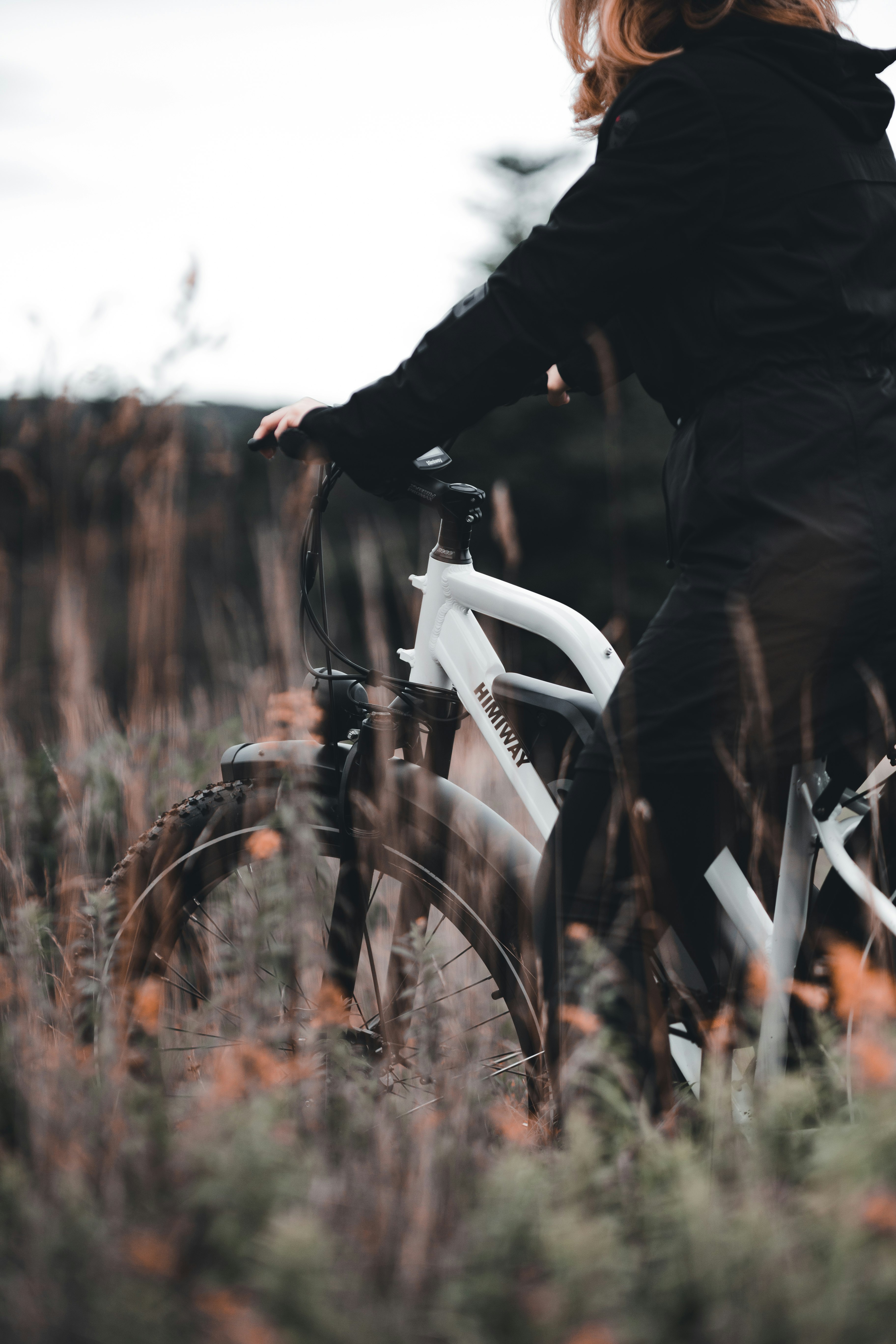 person in black jacket riding white bicycle on brown grass field during daytime